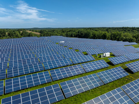 Aerial view of a large solar photovoltaic power plant with rows of solar panels and inverters on a capped landfill under a blue sky. Massachusetts, USA.