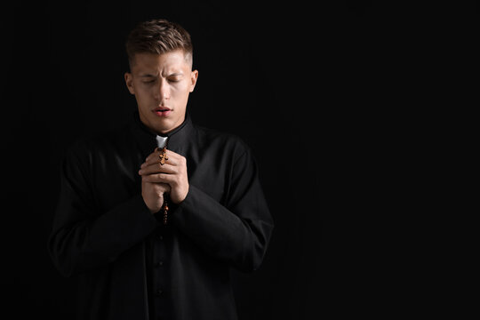 Priest with rosary praying on black background. Space for text