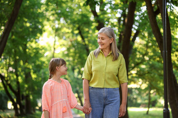 Fototapeta premium Smiling grandmother and granddaughter holding hands while walking in park