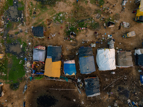 Aerial view of an informal settlement with colorful makeshift shelters, tarpaulin roofs, and scattered debris on dirt ground in Gurgaon, Haryana, India.