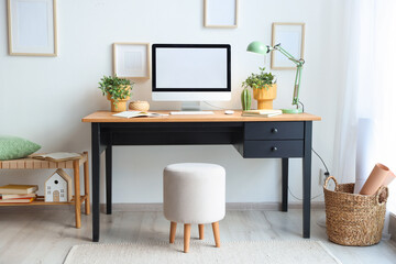 Fototapeta premium Stylish table with computer, houseplants and ottoman near white wall in home office. Interior design