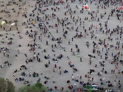 Aerial view of Mertasari Beach crowded with people flying kites on the sandy shore in Denpasar Selatan, Bali, Indonesia.