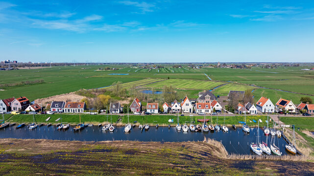 Aerial view of traditional houses lining the waterfront, sailboats moored in the canal, and vast green polder fields in Durgerdam, North Holland, Netherlands.