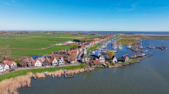 Aerial view of the historic village with traditional houses, a small harbor with moored boats, and green polder landscape in Durgerdam, North Holland, Netherlands.