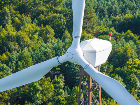 Aerial view of a wind turbine standing amidst a dense green forest in the Kashubia region, Pomeranian Voivodeship, Poland.