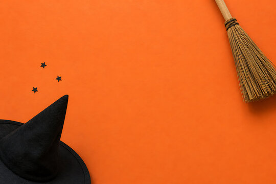 Witch hat and broomstick on bright orange background for halloween greeting card with copy space halloween greeting broomstick background decoration minimalist seasonal celebration creative