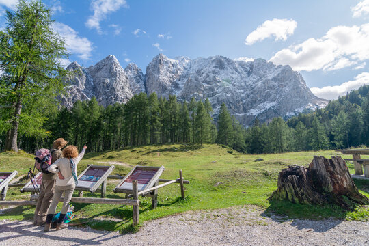 Two hikers admiring the dramatic peaks of the Julian Alps from a scenic viewpoint in Triglav National Park, Slovenia, on a sunny summer day.