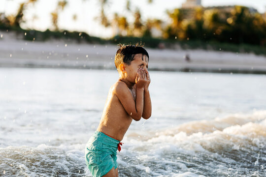 Young Boy Playing in Shallow Ocean Waves on a Sunny Tropical Beach Vacation