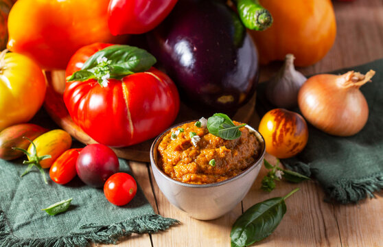 Eggplant caviar in a glass jar and vegetables on a wooden background.