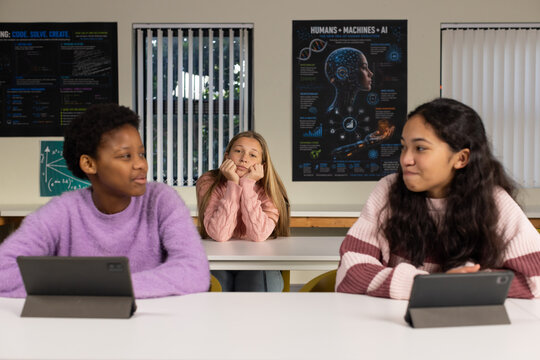 Youth female students sitting in classroom rows using tablets and wearing pastel knit sweaters