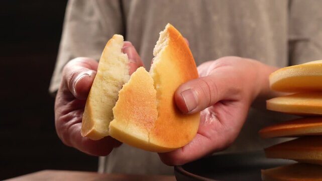 A close-up of hands breaking apart a fresh, golden-brown pancake.