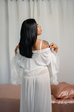 Woman posing in bedroom wearing sheer white nightgown, showing elegant femininity