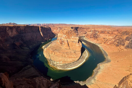 View of Horseshoe Bend with the Colorado River winding through the deep sandstone canyon under a clear blue sky in Page, Arizona, United States.