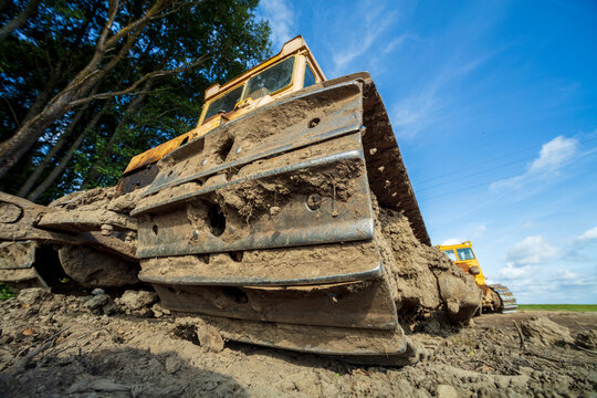 View of a yellow bulldozer with mud-caked metal tracks parked on a construction site under a bright blue sky in Kelme, Siauliai County, Lithuania.