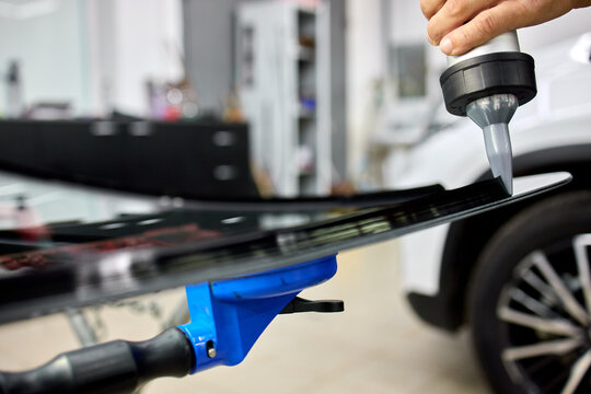Technician polishing glossy black car hood with rotary buffer in bright auto repair workshop under reflective lighting, with car, hood, polishing, technician detail