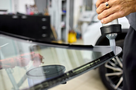 Technician polishing glossy black car hood with rotary buffer in bright auto repair workshop under reflective lighting, with car, hood, polishing, technician detail