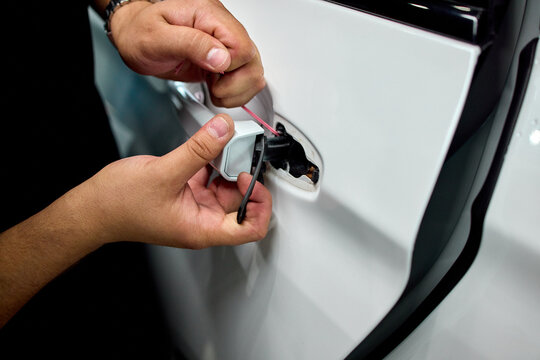 Hands inserting fuel cap into car filler opening beside tethered cap on glossy white body with metal hinge and rubber seal during routine refueling task, with hand, fuel, cap, filler detail