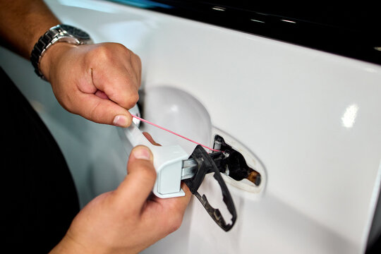 Hands inserting fuel cap into car filler opening beside tethered cap on glossy white body with metal hinge and rubber seal during routine refueling task, with hand, fuel, cap, filler detail