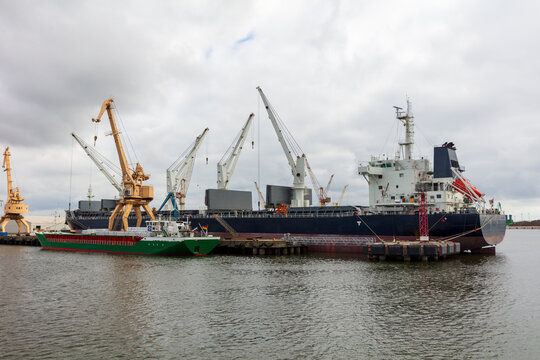 View of cargo ships docked at the Port of Klaipeda with large yellow cranes under a cloudy sky in Klaipeda, Klaipeda County, Lithuania.