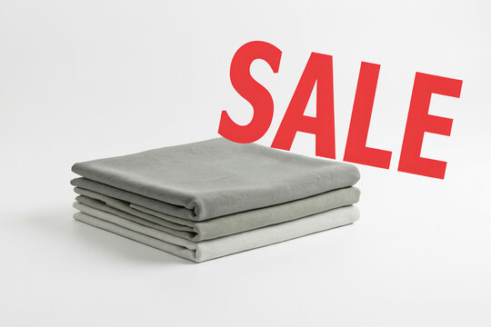 A stack of neatly folded plain gray fabrics with the prominent bold red uppercase SALE text displayed above them announcing a special discount and promotional offer for potential customers shopping
