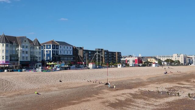 Bognor Regis West Sussex England UK. 14.07.2026. Video. A wide shot of a bustling pebble beach on a clear day, featuring diverse architecture and individuals relaxing by the sea at Bognor Regis 