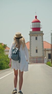 Young woman with backpack and summer hat walking toward Cabo Carvoeiro Lighthouse in Peniche, Portugal