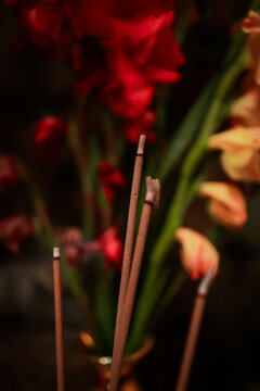 View of burning incense sticks in a temple at The Marble Mountains with blurred red and yellow flowers in the background in Da Nang, Da Nang, Vietnam.