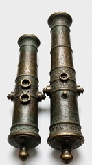 Naklejka premium Two antique bronze cannons stand upright on white surface. Historic metal weapons feature ornate patterns, weathered texture. Vintage artillery pieces represent naval technology from past war times.