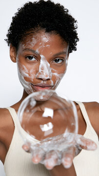 Young black woman with facial cleanser foam on her skin, holding out a large soap bubble, symbolizing purity, refreshing, and daily skincare routine for clear, healthy skin
