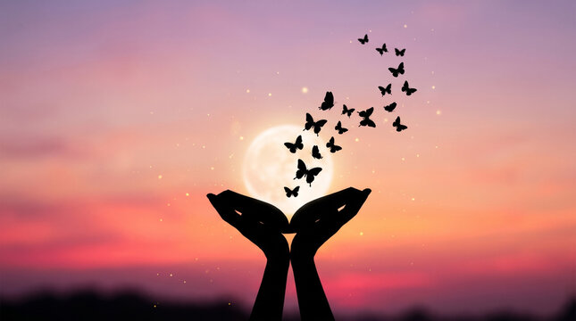 Silhouette hands releasing magical butterflies against a glowing sunset and full moon
