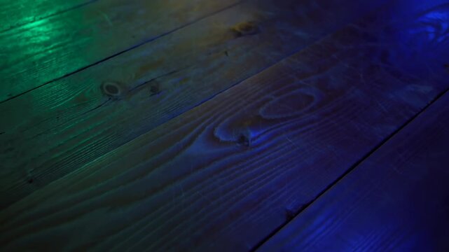 Colored gel lighting crossing diagonal wooden planks with pronounced grain, knots, seams, nail heads, and glossy highlights in moody close-up with cool green, teal, blue tones