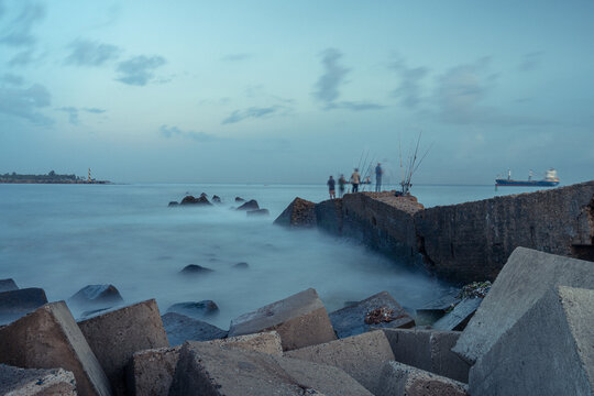 View of fishermen standing on a concrete breakwater with tetrapods at dusk, with a ship in the distance in San Pedro de Macoris, San Pedro de Macoris, Dominican Republic.