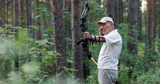 Senior man practicing archery with compound bow in forest