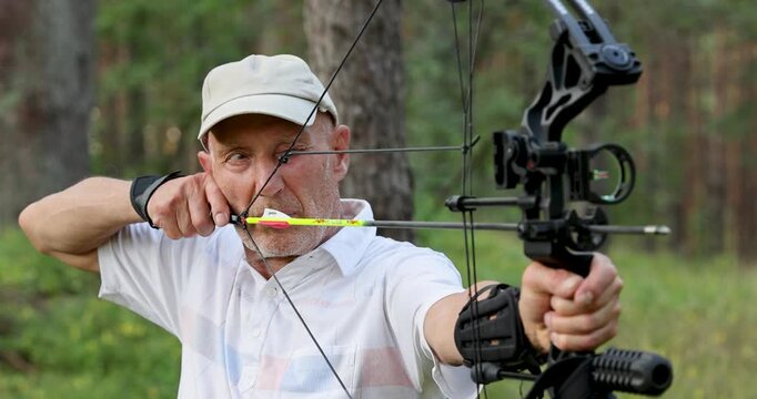 Senior man practicing archery with compound bow in forest