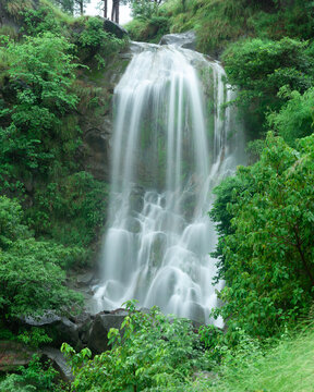 View of a waterfall cascading over a rocky cliff surrounded by lush green vegetation along the roadside in Kotli, Azad Kashmir, Pakistan.