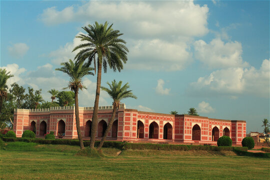 View of the historic Tomb of Noor Jahan with its red sandstone facade, arched entrances, and tall palm trees set against a blue sky in Shahdara, Punjab, Pakistan.