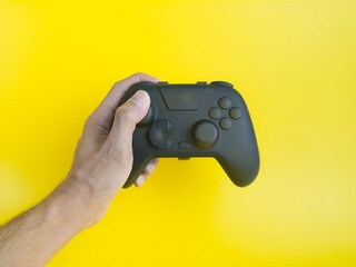 First person view of hand holding a blank black gaming controller on yellow background.  © wibiwisnu