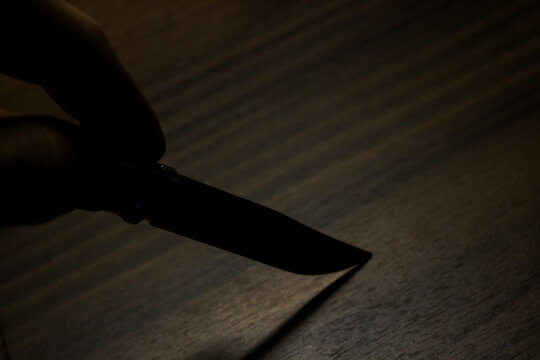 an old rusty knife with wooden handle getting hold in hand in front of a wooden background leaving a shadow