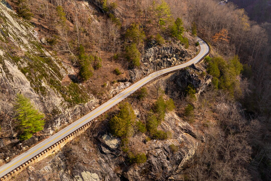 Scenic mountain road in North Carolina Highlands region. Parkway curves beneath golden trees and steep rocky slopes in fall season