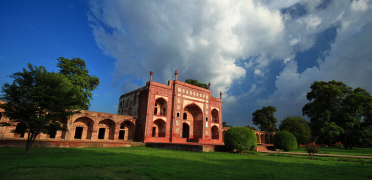 View of the historic Tomb of Jahangir with its intricate red sandstone architecture and arched gateways set against a dramatic cloudy sky in Lahore, Punjab, Pakistan.