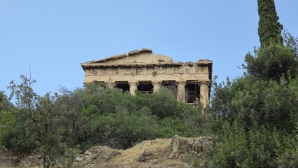 Fototapeta premium Athens, Greece - 8 July 2026. Temple of Hephaestus in the Ancient Agora seen above olive trees and shrubs, with Doric architectural columns, interior scaffolding, a cypress tree, and clear sky.