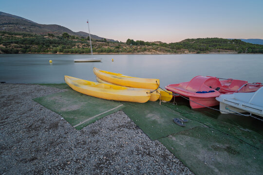 Yellow kayaks and red pedal boats on beznar reservoir water, granada, offering recreation and watersports in nature