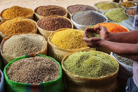 View of a merchant holding and pouring various colorful grains and legumes from large sacks at the historic Akbari Mandi grain market in Lahore, Punjab, Pakistan.
