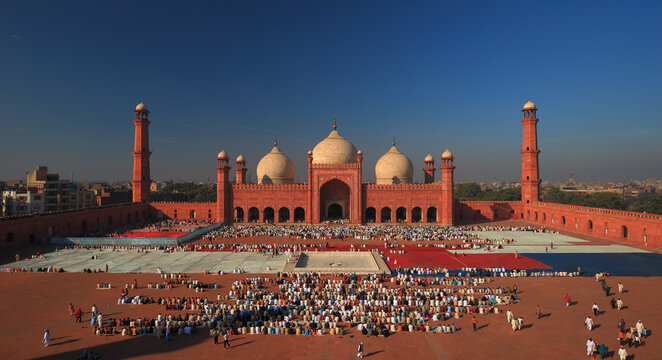 View of Badshahi Mosque with a large crowd of people gathered in the courtyard for prayer under a clear blue sky, Lahore, Punjab, Pakistan.