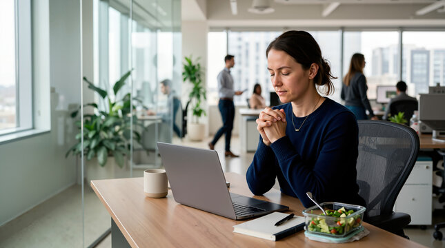 Businesswoman praying at her desk in a modern office. Female corporate employee with clasped hands taking a moment of reflection before lunch. Faith and mindfulness at workplace concept