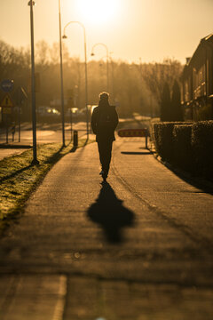 Silhouette of person walking along suburban path during sunrise creating long shadow and calm mood.