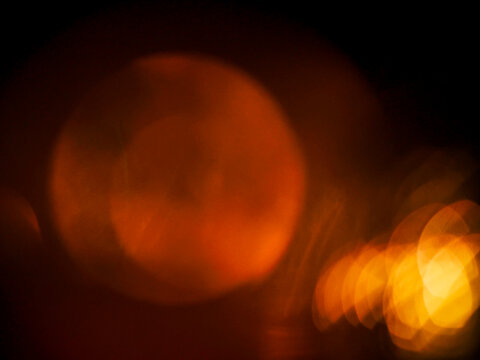 Abstract bokeh background with warm orange and yellow light circles on black. Blurred glowing orbs create soft, dreamy visual effect. Light leaks for design and special effects.
