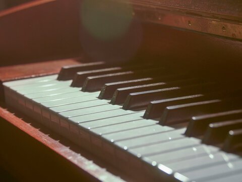 Piano keys under warm, soft lighting. Shallow depth of field highlights keyboard texture. Wooden casing partially visible in background. Focus on black and white keys with gentle blur