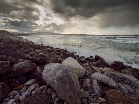Dark storm clouds hover over wild ocean, . Waves crash against rocky shore. Turbulent water flows toward distant hills. Nature power displayed in dramatic weather. Strandhill beach, Sligo, Ireland.