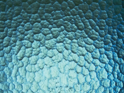 Close up of textured blue surface with repeating polygonal patterns. Natural material with aged, cracked appearance. Organic, symmetrical design suitable for backgrounds